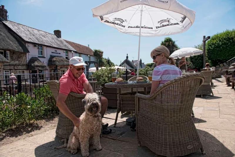 A couple and their dog enjoy the terrace at Smugglers Inn, a dog-friendly pub in Dorset