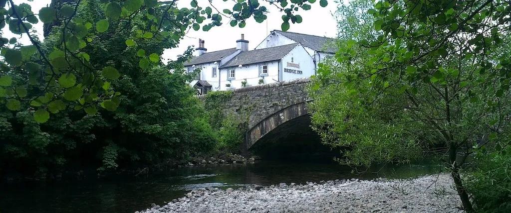 A view through lush trees and over the bridge of Bridge Inn, a dog-friendly pub in the Lake District