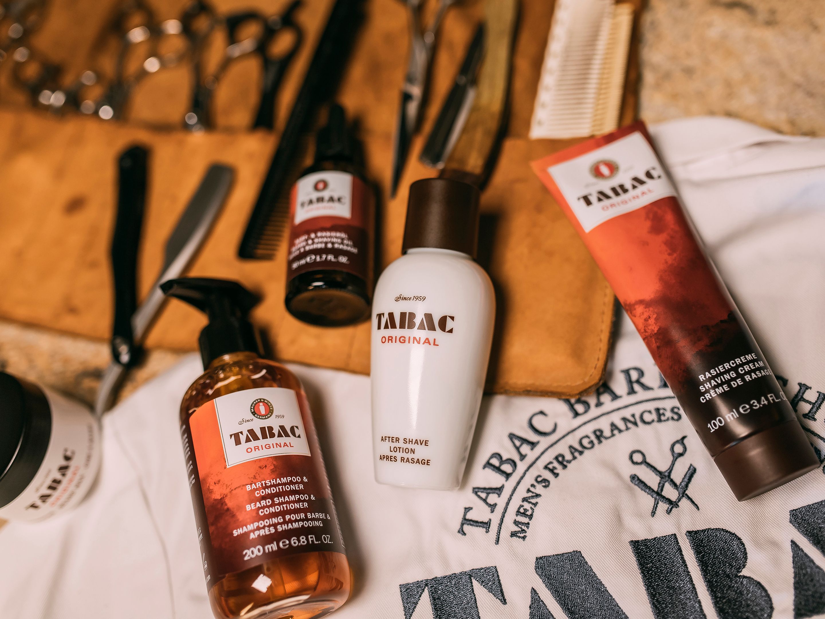 Tabac Original aftershave, beard shampoo, and shaving cream surrounded by barber tools.