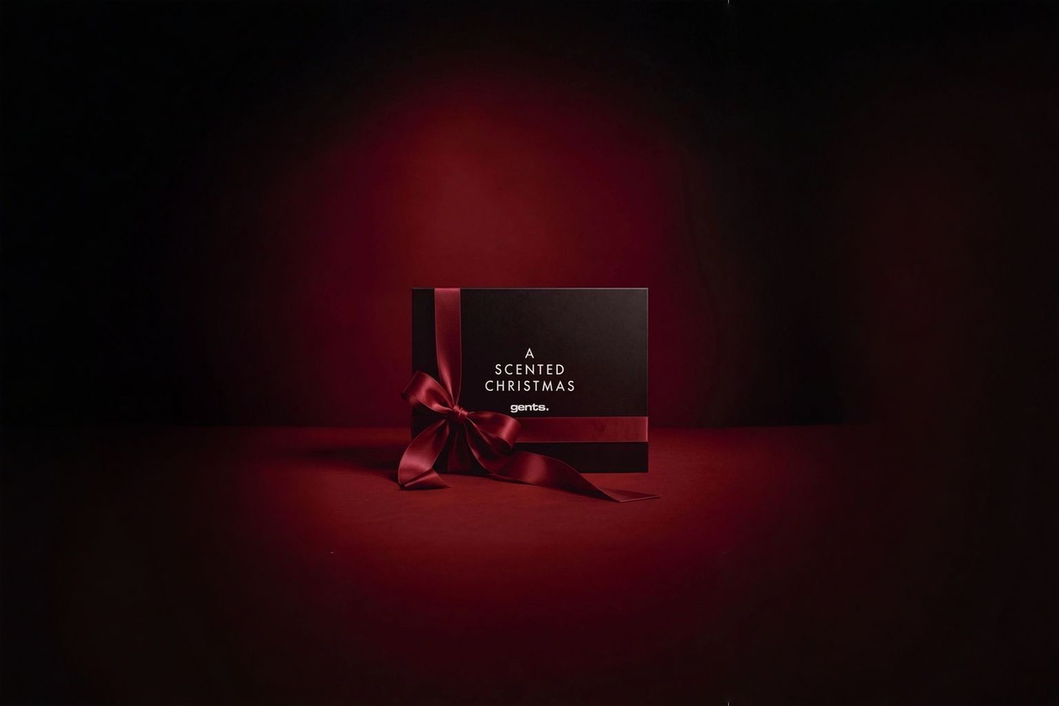 Schwarze Geschenkbox mit roter Schleife und der Aufschrift „A Scented Christmas“ vor dunkelrotem Hintergrund.