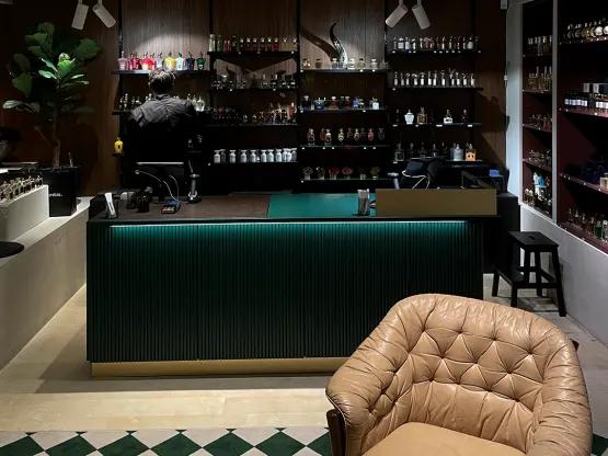 Et duftbutiksinteriør med en mørkegrøn oplyst disk, hylder fyldt med parfume­flasker og en beige knapstukket lænestol i læder.