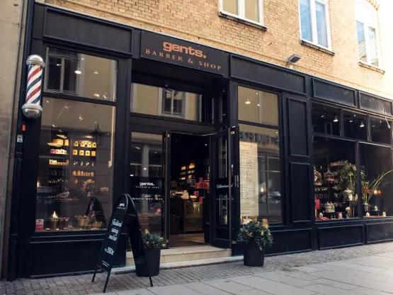 En sort herrebutik med en barberstang og produkter synlige i vinduerne