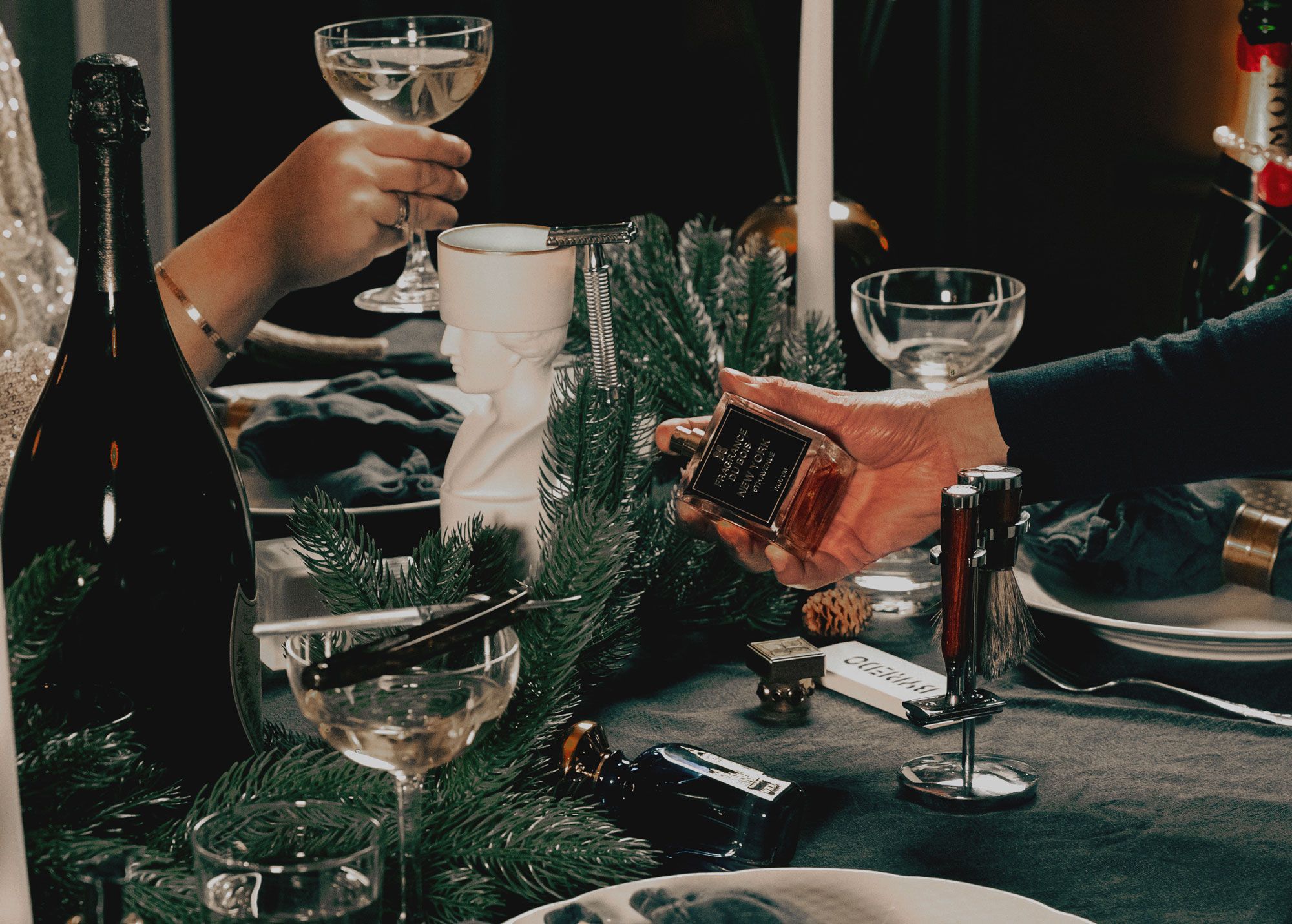 Ein Mann, der ein Parfüm an einem gedeckten Tisch mit Tannenzweigen hält