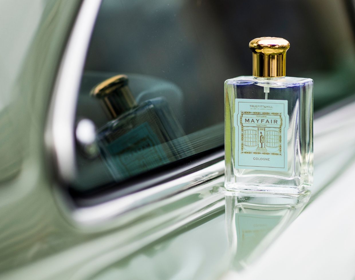 En flaska Truefitt & Hill Mayfair Cologne med guldfärgad kork på en ljusgrön bil.