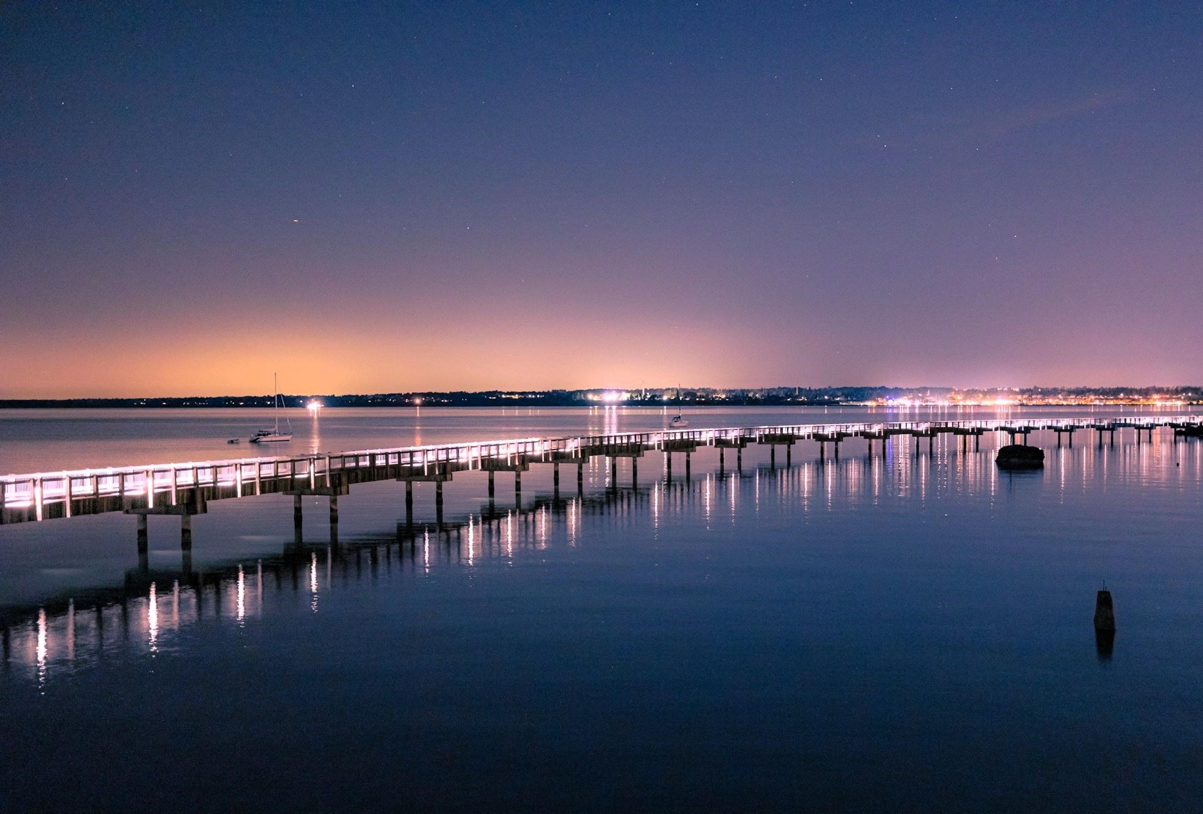 A tranquil night scene at Taylor Dock in Bellingham, Washington, where the calm waters reflect the gentle glow of the lights along the dock.