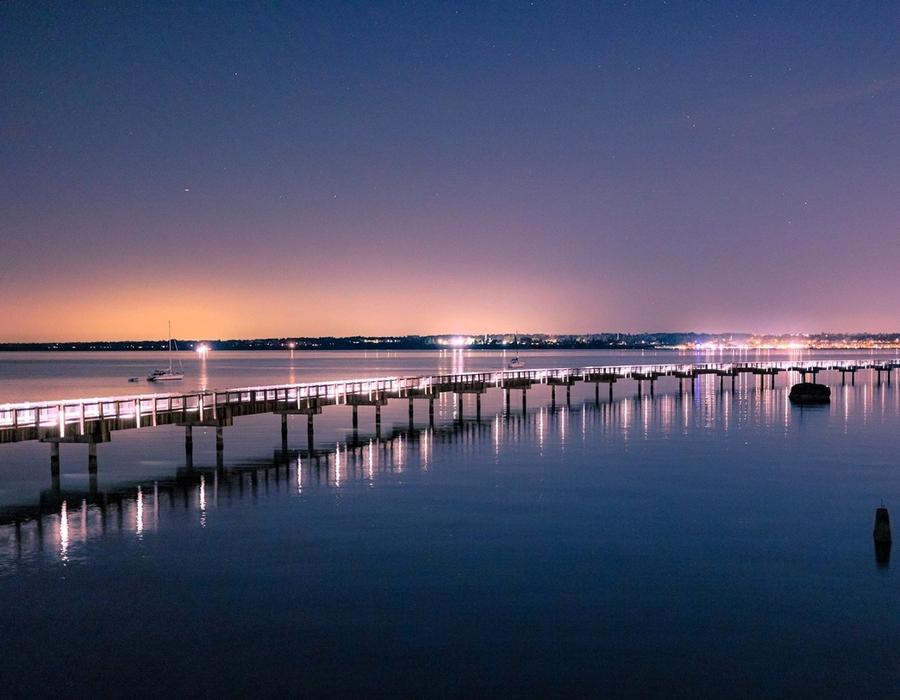 A tranquil night scene at Taylor Dock in Bellingham, Washington, where the calm waters reflect the gentle glow of the lights along the dock.