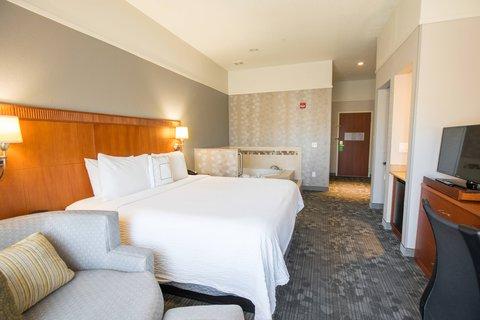 Photo of Courtyard Merced - A spacious room featuring a large bed, a private whirlpool tub, a sitting area with a chair and table, and a bathroom with a bathtub and shower.