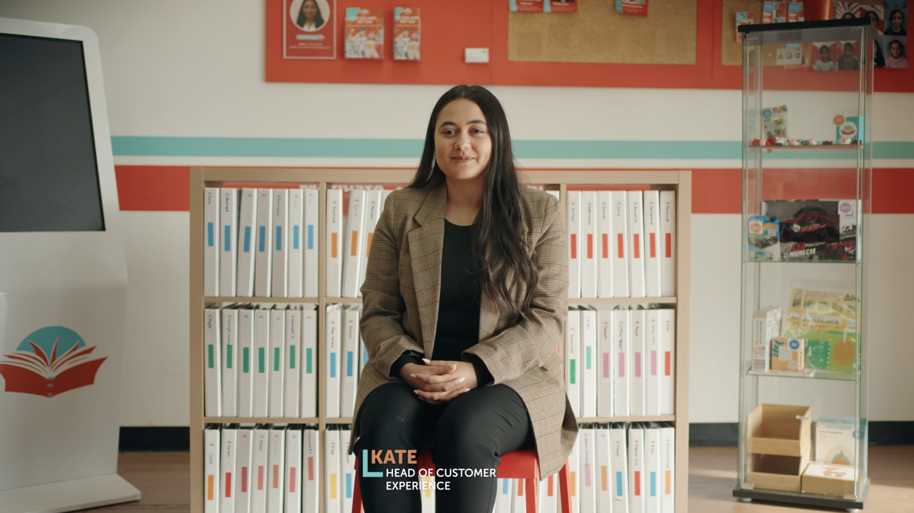 a woman sitting in front of a bookshelf with kate head of customer experience written on her knee