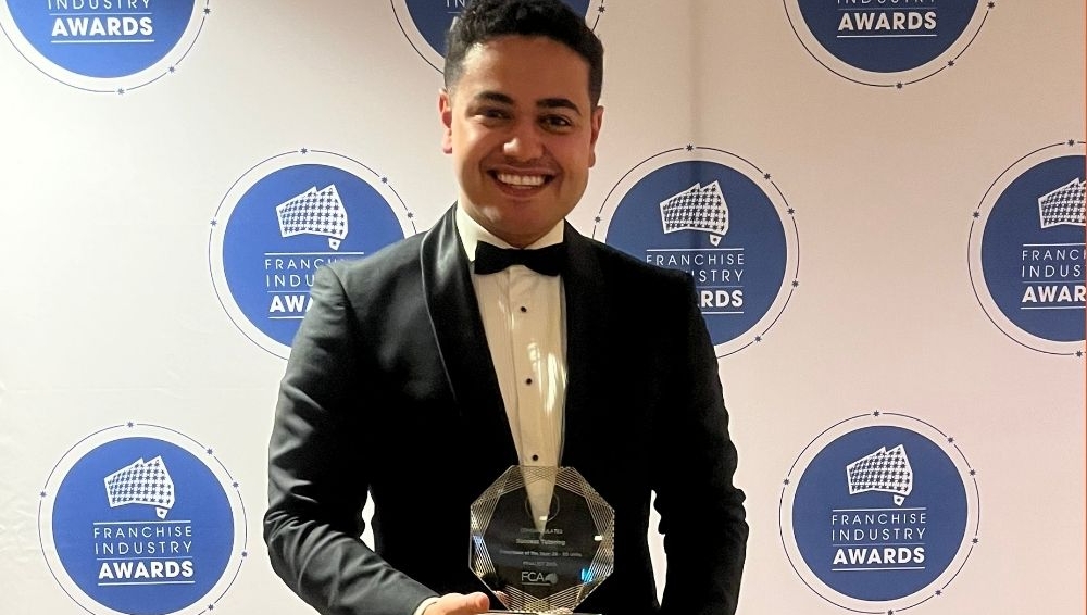 a man in a tuxedo is holding a trophy in front of a wall of awards .