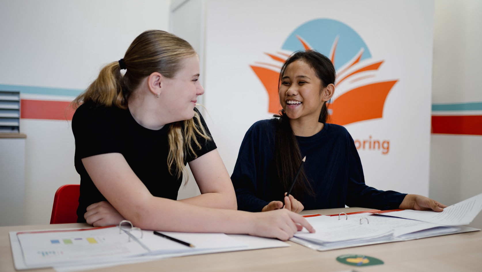two girls sit at a table in front of a wall that says learning