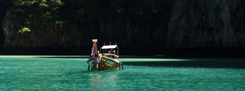 Traditional Thai longtail boat with colorful ribbons anchored in crystal-clear turquoise waters, surrounded by dramatic limestone cliffs in Thailand.