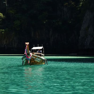 Traditional Thai longtail boat with colorful ribbons anchored in crystal-clear turquoise waters, surrounded by dramatic limestone cliffs in Thailand.