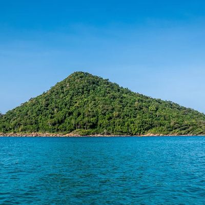 A lush green island surrounded by turquoise waters under a clear blue sky in Cambodia, showcasing the serene beauty of Koh Rong or Koh Rong Samloem.