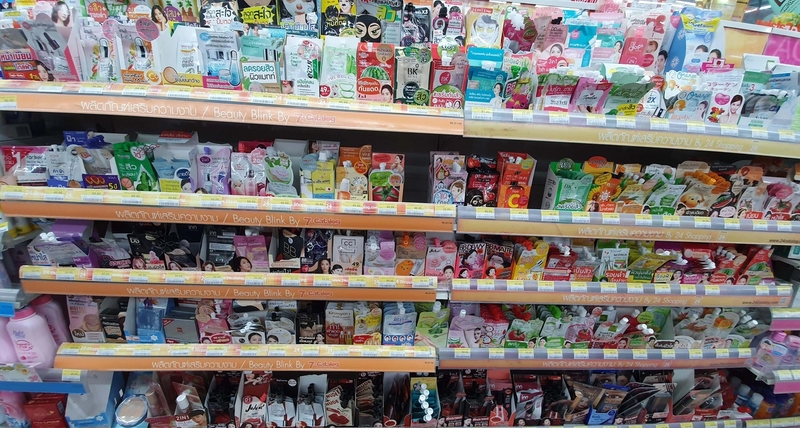 Shelf with beauty products at 7-Eleven in Thailand, featuring popular Asian skincare and cosmetics, including facial masks, serums, and sunscreens.
