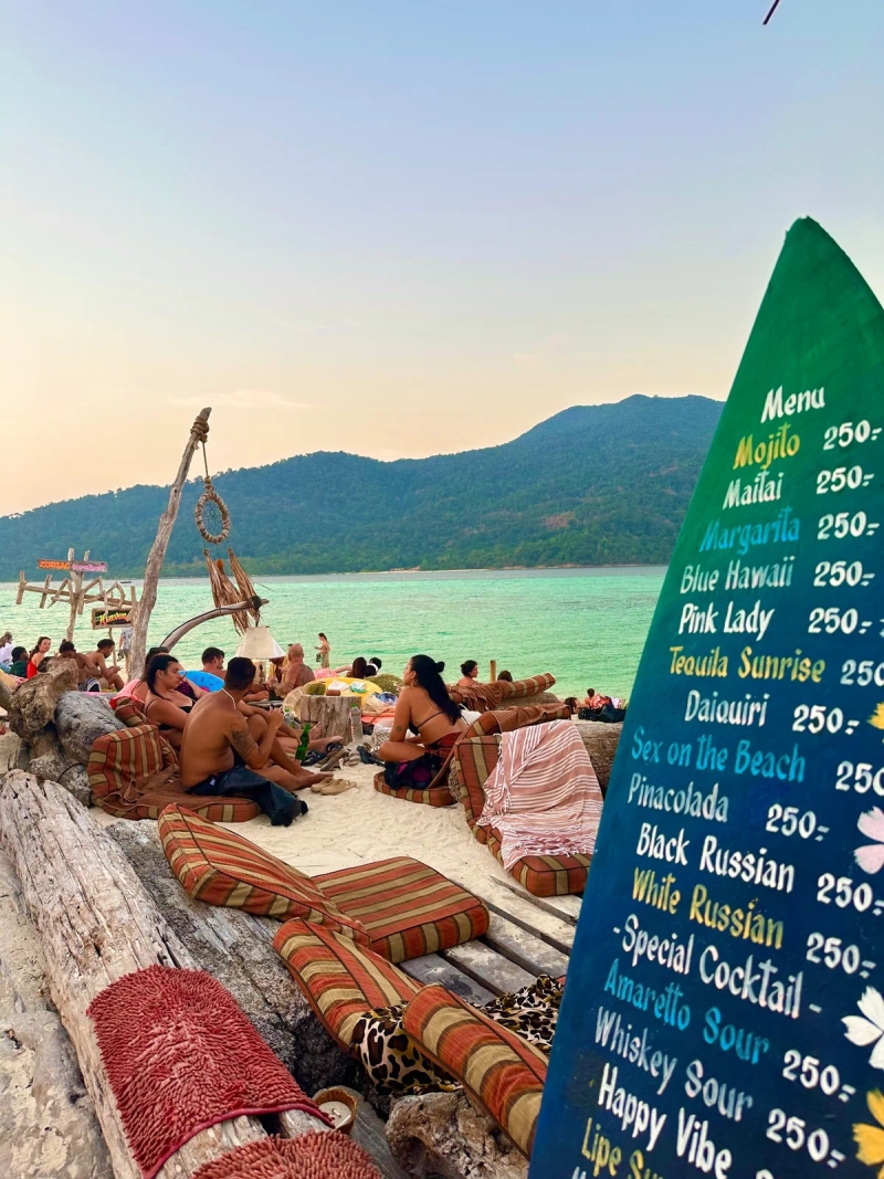 Beach bar with colorful cushions and a cocktail menu on Sunset Beach, Koh Lipe, Thailand, with turquoise water in the background