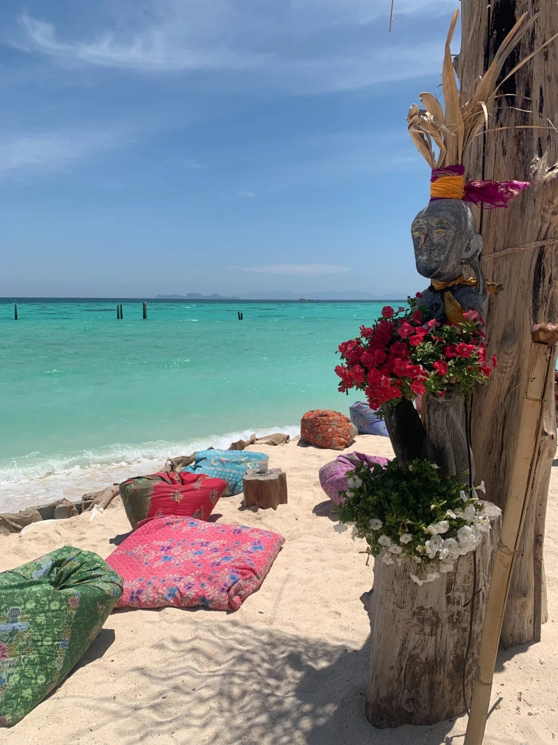 Clear turquoise water and colorful beach cushions at Koh Lipe’s North Point Beach, surrounded by tropical plants and a serene atmosphere. Ideal place for sunbathing and relaxing by the sea.