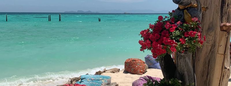 Clear turquoise water and colorful beach cushions at Koh Lipe’s North Point Beach, surrounded by tropical plants and a serene atmosphere. Ideal place for sunbathing and relaxing by the sea.