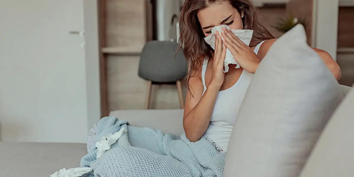 Person sneezing and using a tissue, experiencing allergy symptoms indoors. Image highlights the importance of air filtration for reducing allergens in the home.