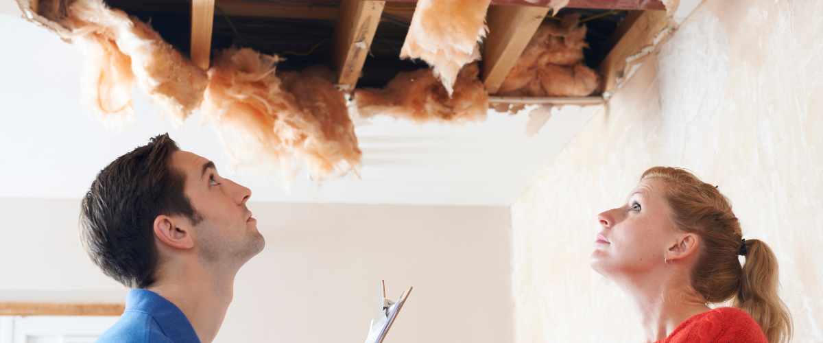 Homeowners inspecting water damage in the ceiling, highlighting the importance of proper HVAC drainage and system protection to prevent costly repairs.