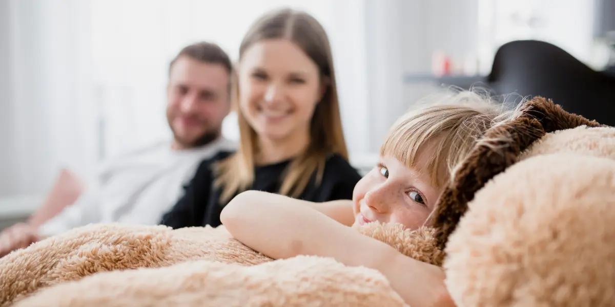 A happy family relaxing indoors in a comfortable climate, thanks to an Energy Recovery Ventilator provided by SS&B Heating & Cooling in Springfield, MO. A little girl cuddles her stuffed animal, symbolizing the comfort and peace of mind that comes with quality HVAC systems.