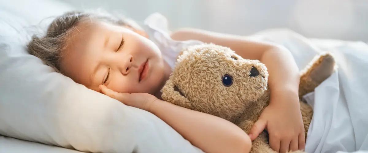 Young child peacefully sleeping in bed while hugging a teddy bear. This image represents safety, comfort, and a secure environment, highlighting the importance of home safety products like carbon monoxide detectors.