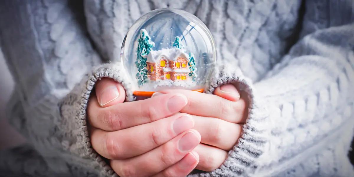 Hands holding a snow globe with a cozy, snow-covered house inside, symbolizing warmth, comfort, and the safety of a well-heated home.