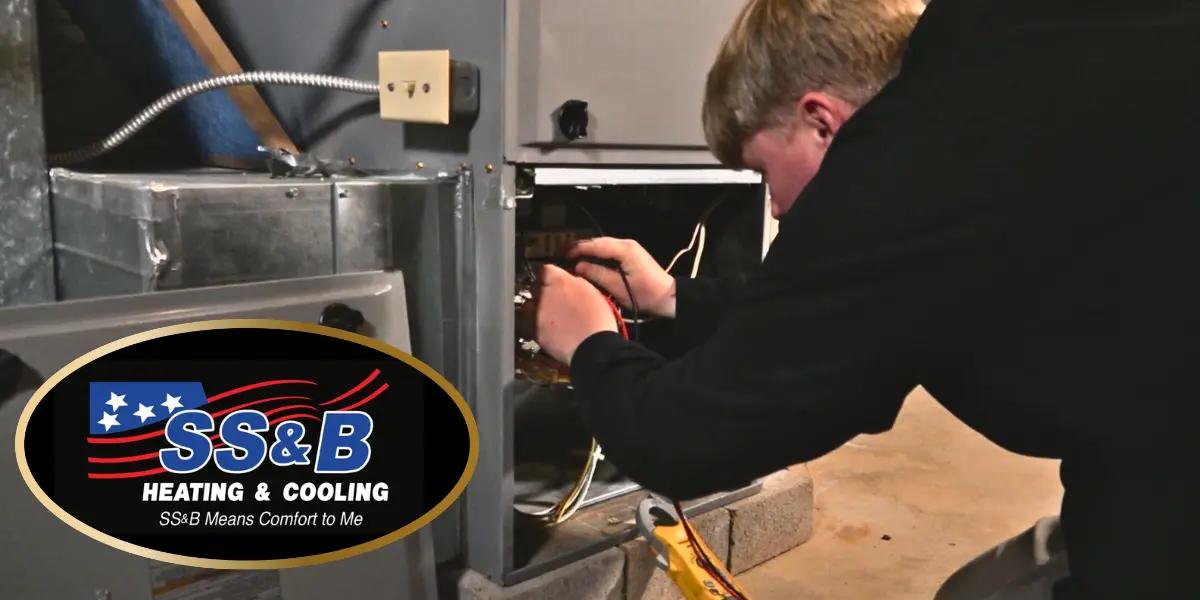 SS&B Heating & Cooling technician performing maintenance on a furnace, ensuring proper functionality. SS&B Heating & Cooling logo is displayed, with the tagline 'SS&B Means Comfort to Me.