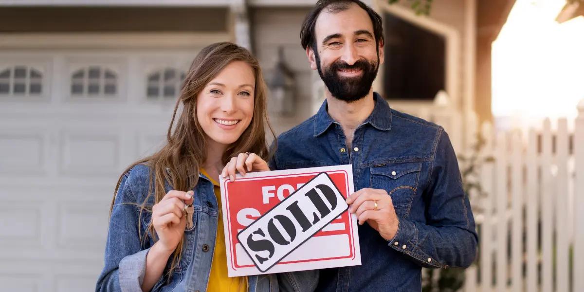A joyful couple holding a sold sign and keys in front of their new home in Springfield, MO.