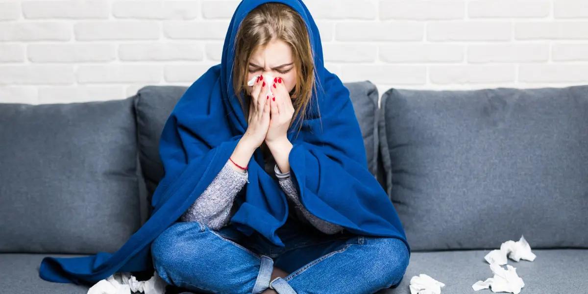 Lady indoors suffering from the flu, sneezing and holding a tissue, depicting the importance of maintaining good indoor air quality during flu season.