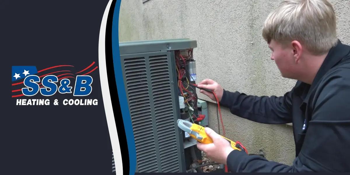 Technician from SS&B Heating & Cooling in Springfield, MO, performing maintenance on an outdoor air conditioning unit, using a multimeter to check electrical connections.