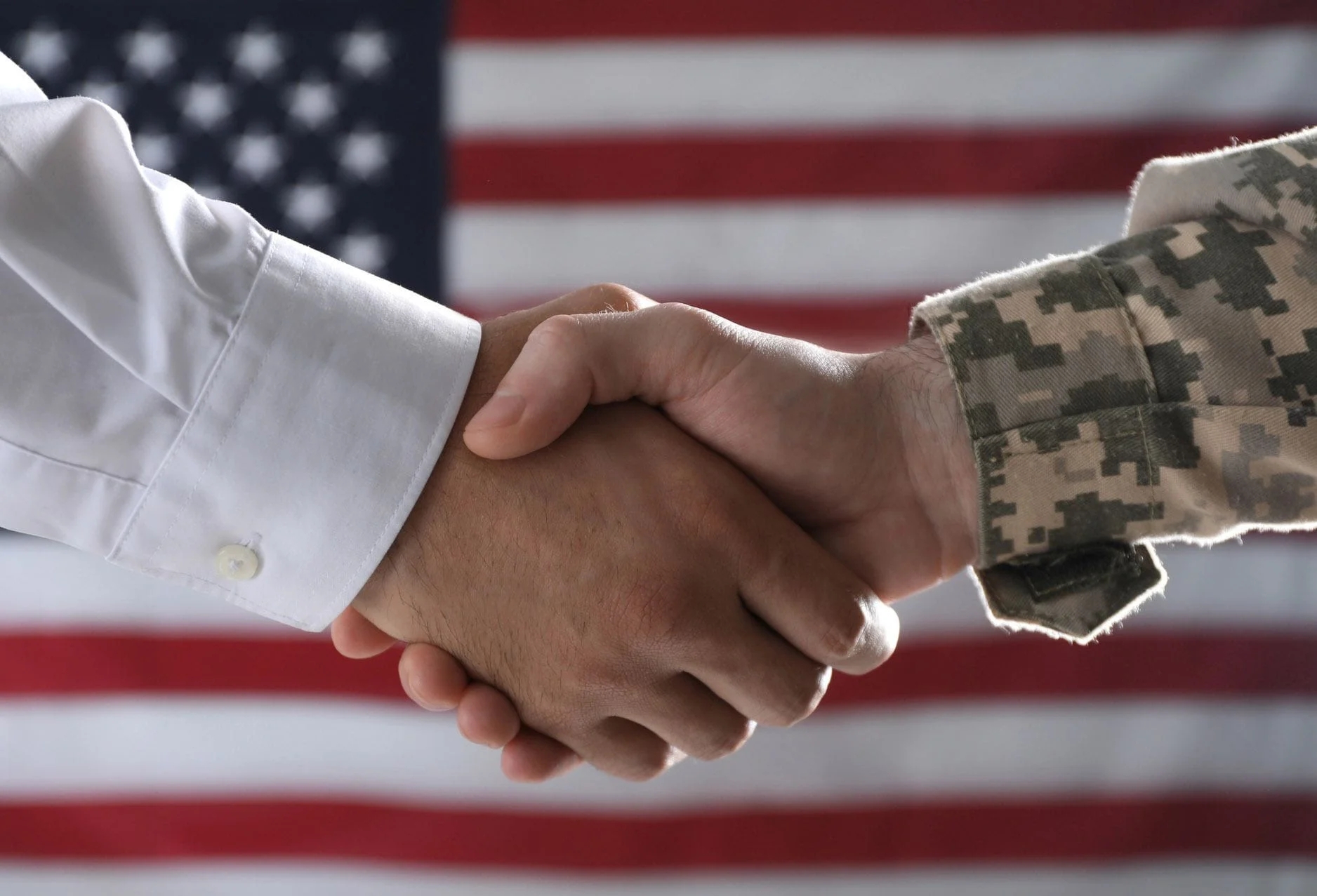 A civilian and a service member shaking hands in front of a U.S. flag