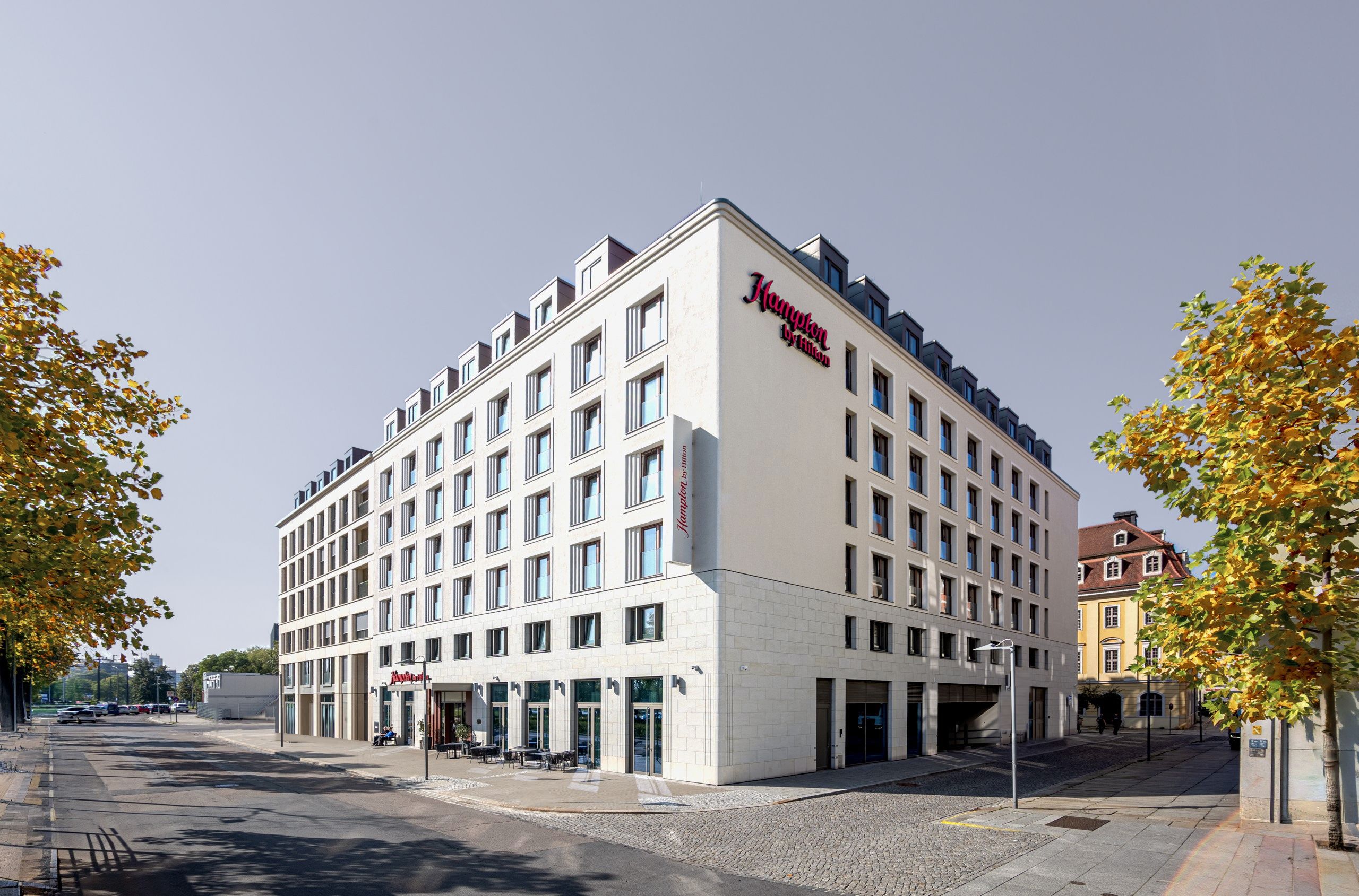 Hampton by Hilton Dresden – Eckansicht aus Fußgängerperspektive: das weiße Hotel nach Entwurf von KLM, links im Block und am rechten Bildrand Nachbarbauten (nicht von KLM)
