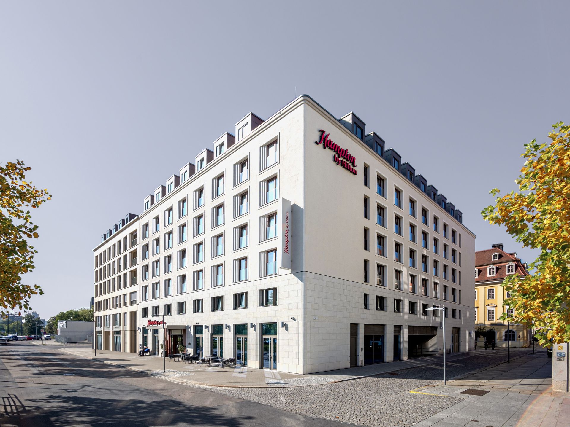 Hampton by Hilton Dresden – Eckansicht aus Fußgängerperspektive: das weiße Hotel nach Entwurf von KLM, links im Block und am rechten Bildrand Nachbarbauten (nicht von KLM)