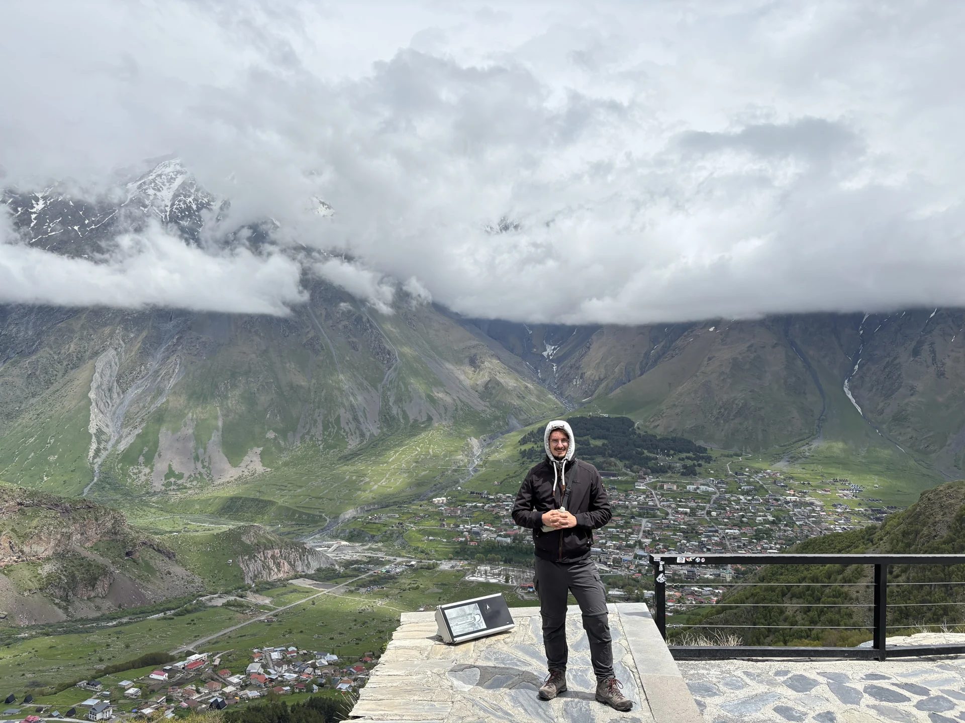 Kevin in Wanderkleidung an einem Aussichtspunkt über einem Tal mit wolkenverhangenen Bergen