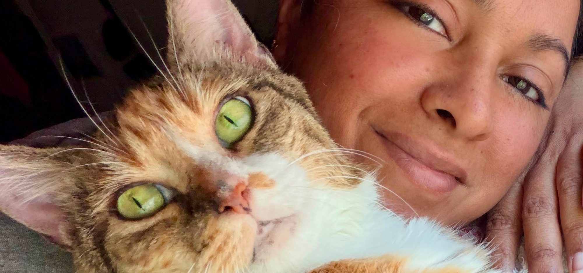 Linsy John resting her head beside a green-eyed tabby cat.