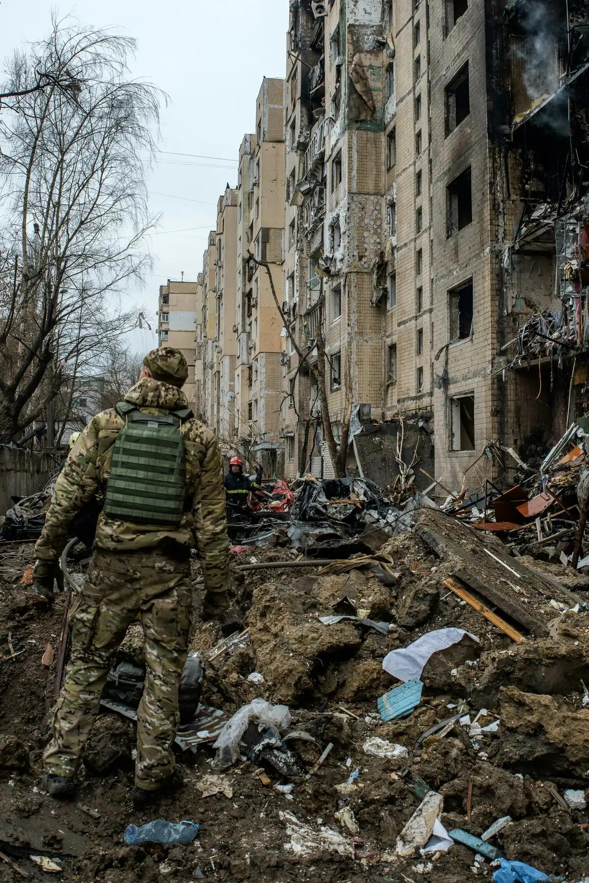 En soldat og en brannmann i ruinene foran en bombet boligblokk