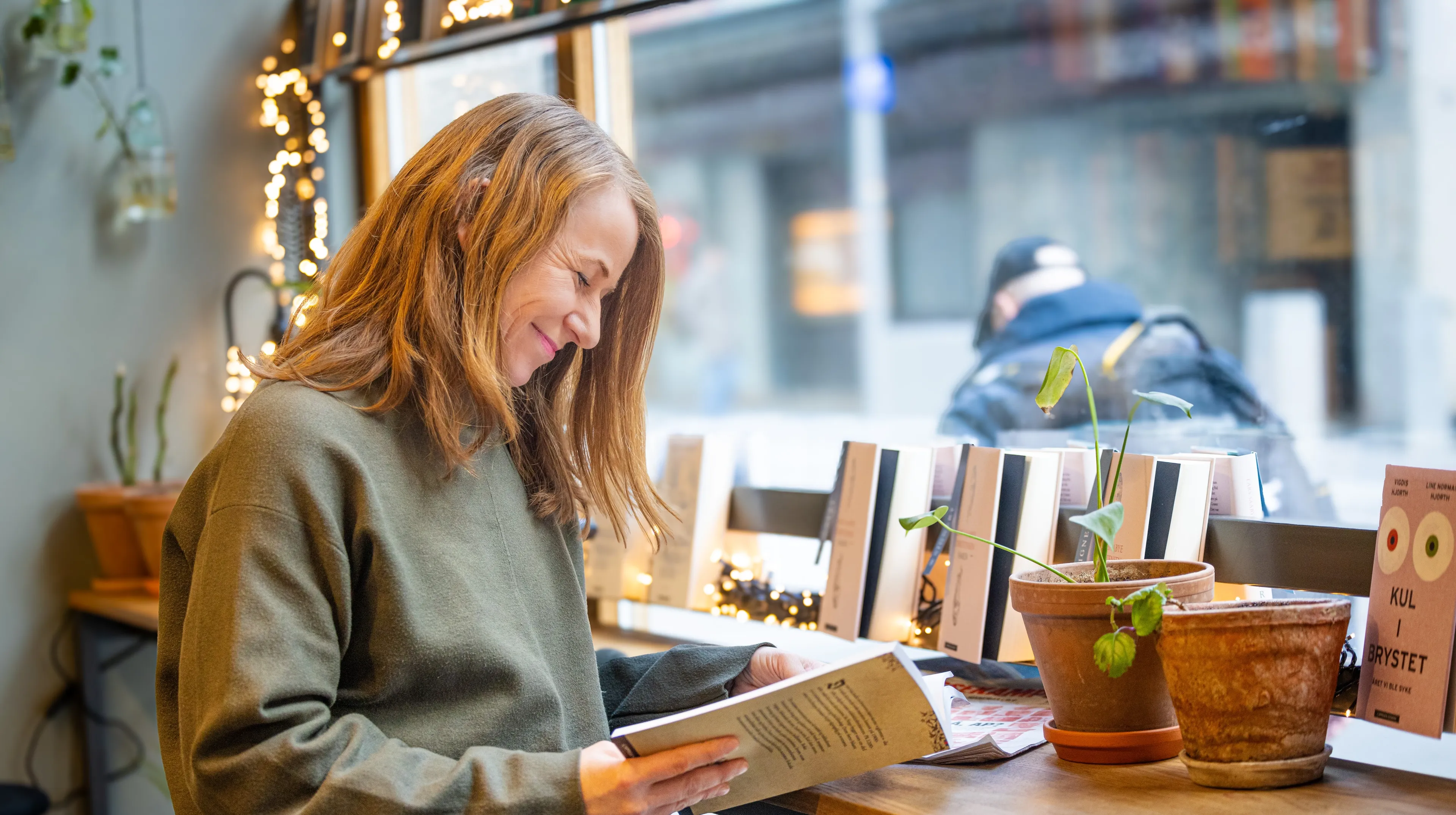 Kvinne sitter i vinduet i en bokhandel og blar i en lærebok