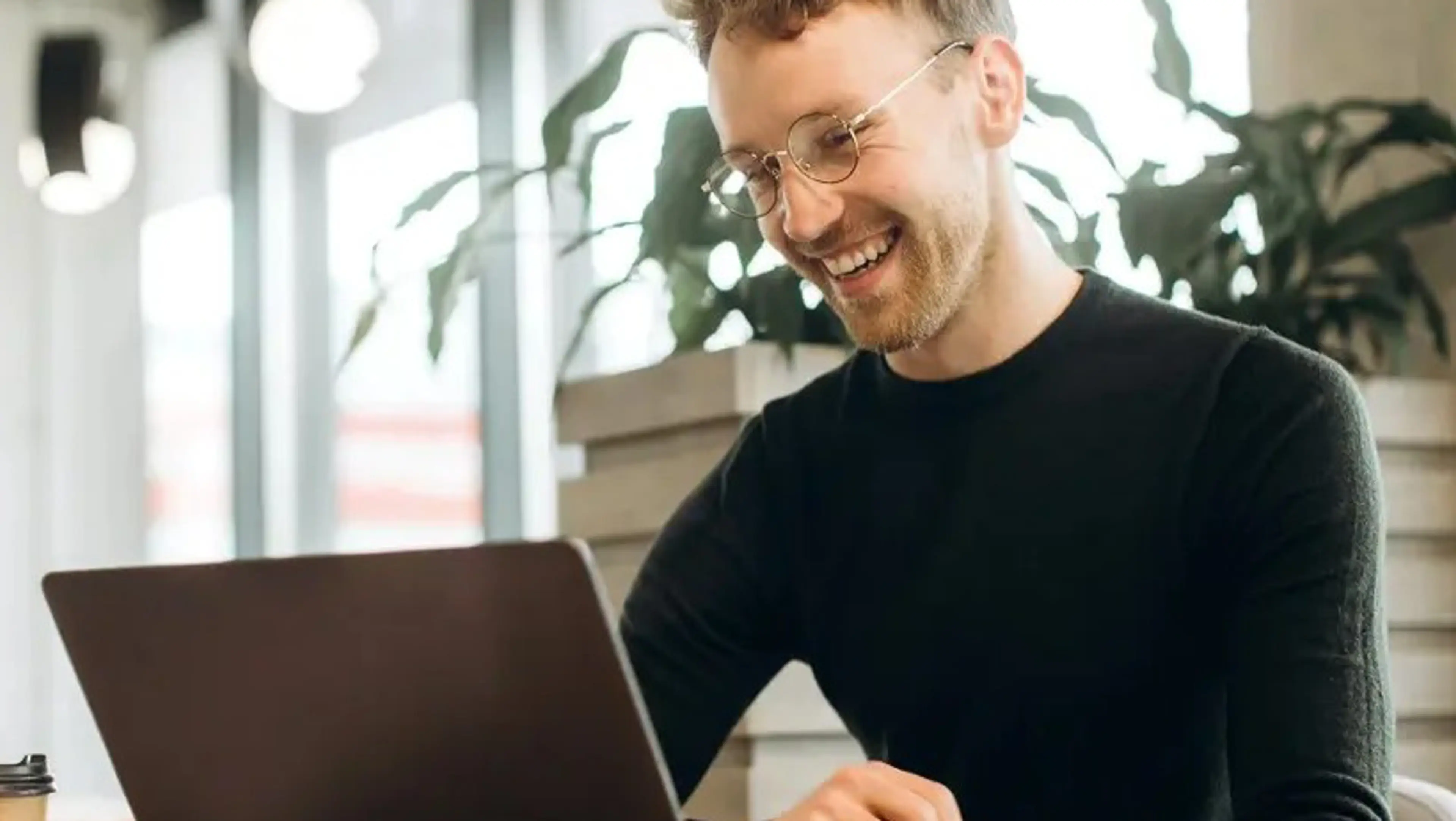 Mannlig student i svart genser som smilende ser på en pc-skjerm