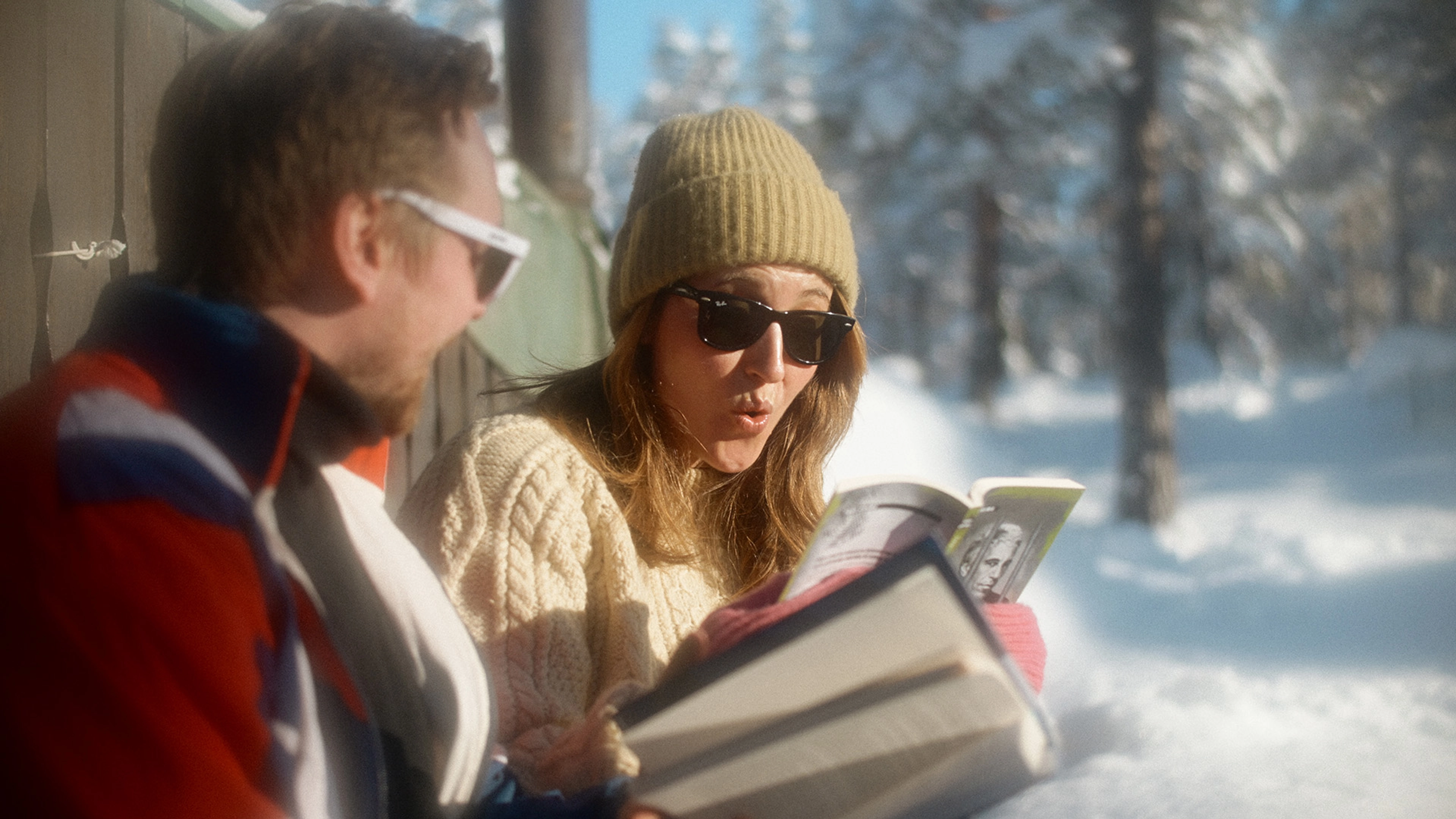 En mann og en kvinne leser i solveggen på en hytte. Kvinnens ansiktsuttrykk tyder på at hun leser noe spennende.