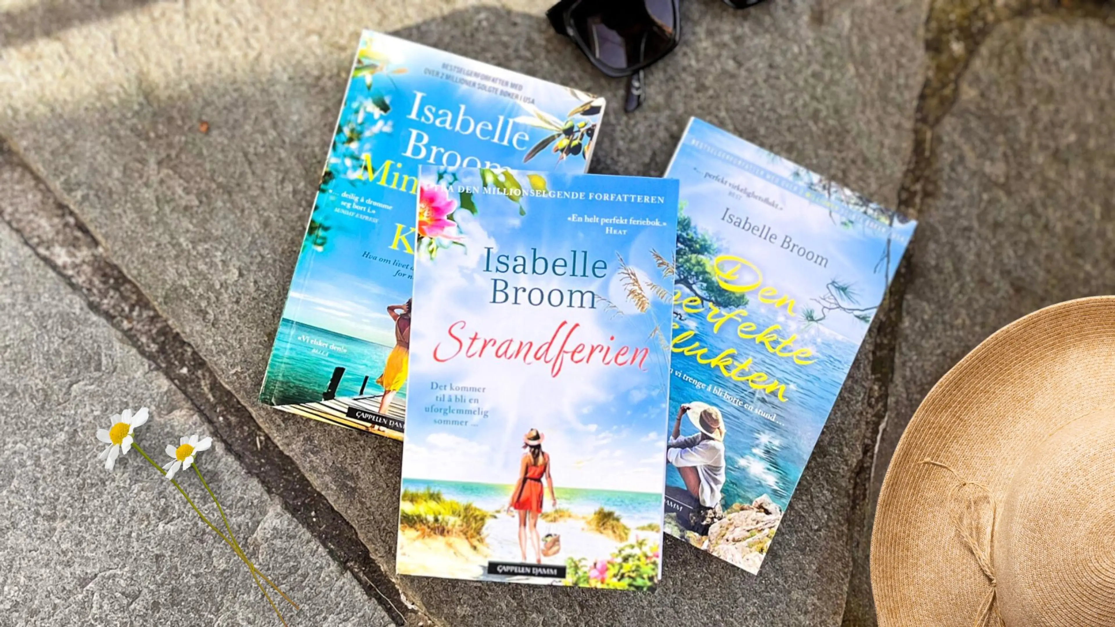 Tre bøker av Isabelle Broom liggende på steinheller med solbriller og solhatt ved siden av