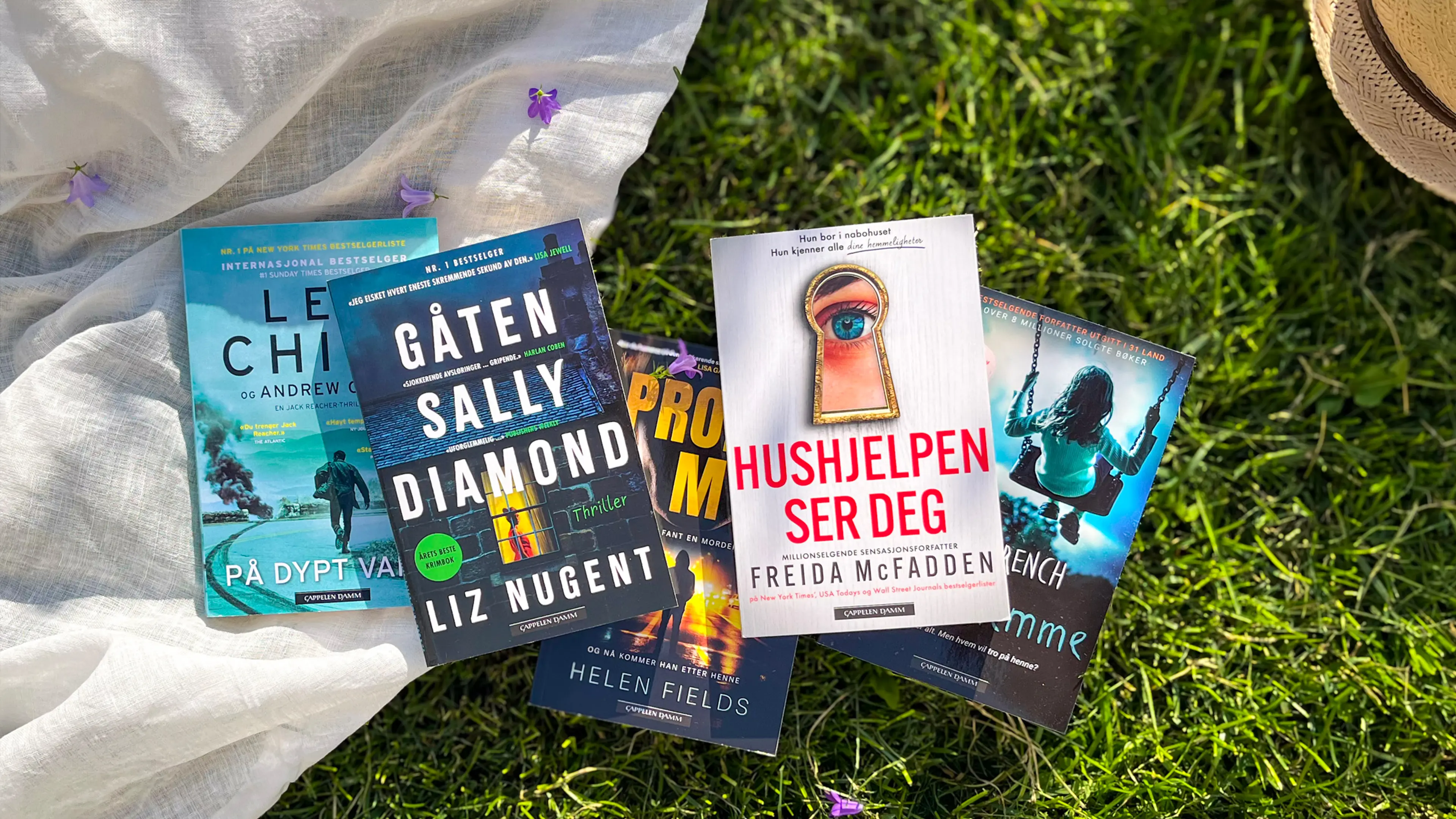 Fem krimbøker som ligger på en gressplen, delvis på et håndkle