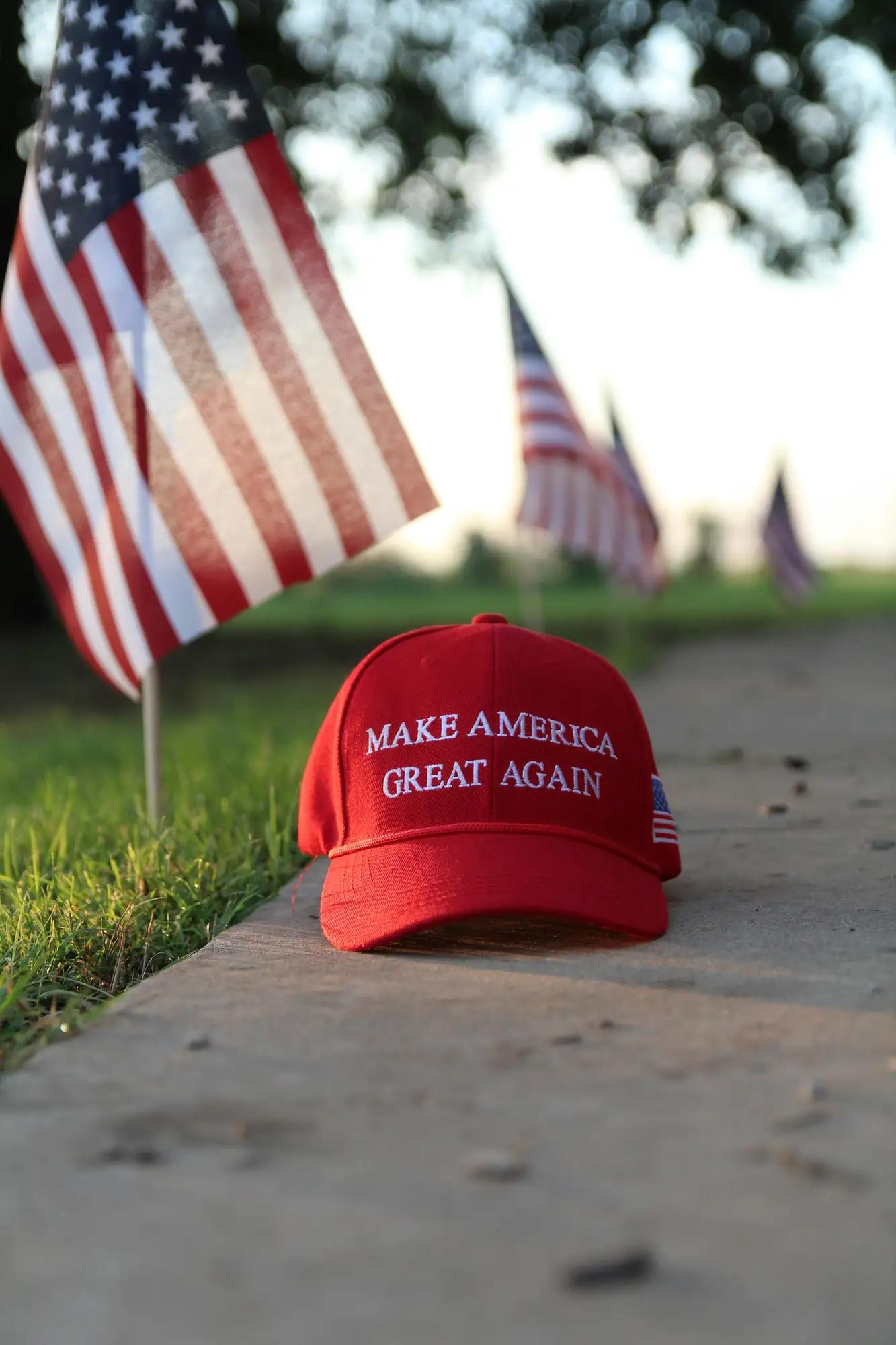 En rød «Make America Great Again»-caps på fortauet, med amerikanske flagg bak