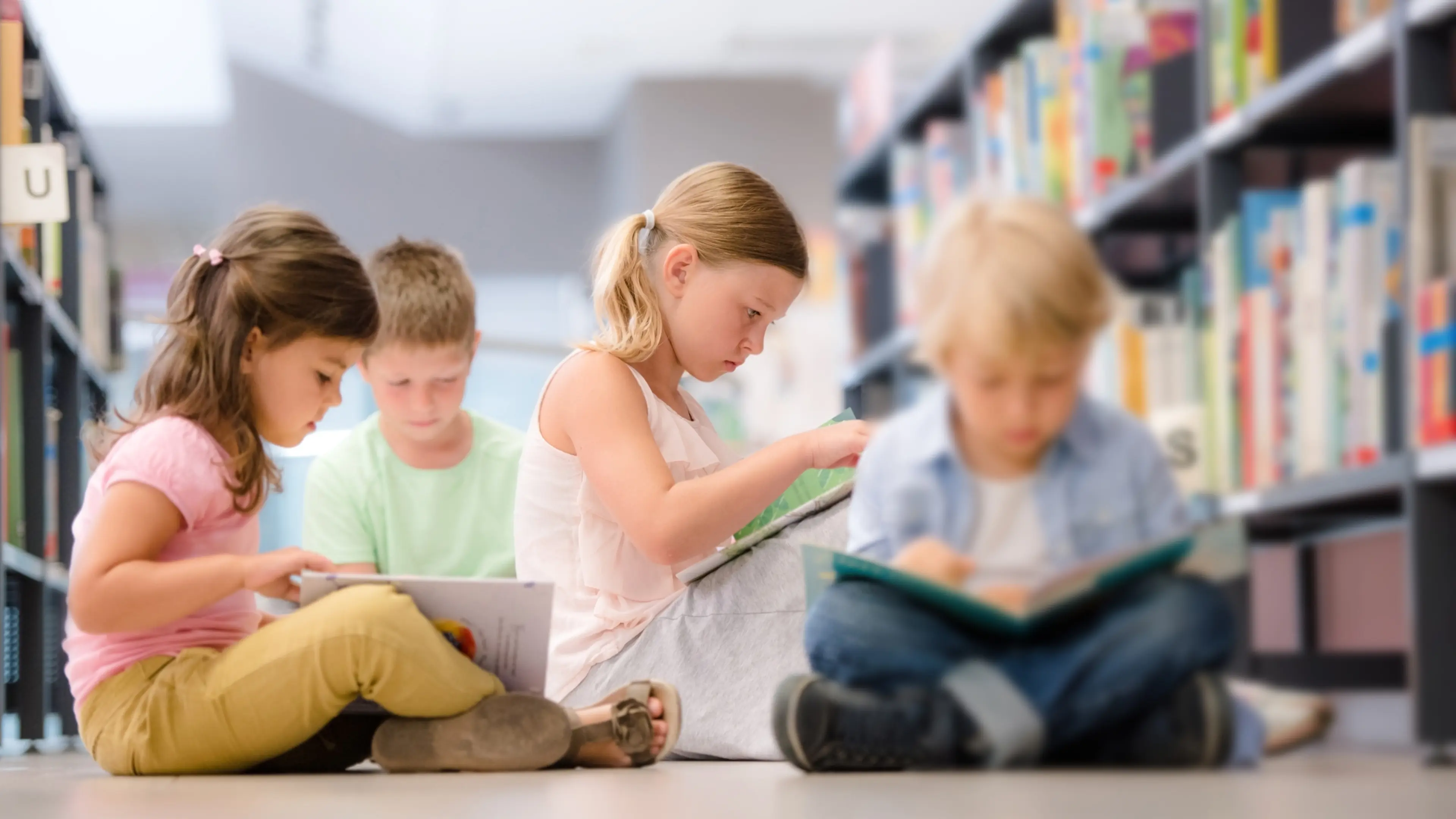 Fire barn som sitter på gulvet mellom bokyller i biblioteket og leser i hver sin bok