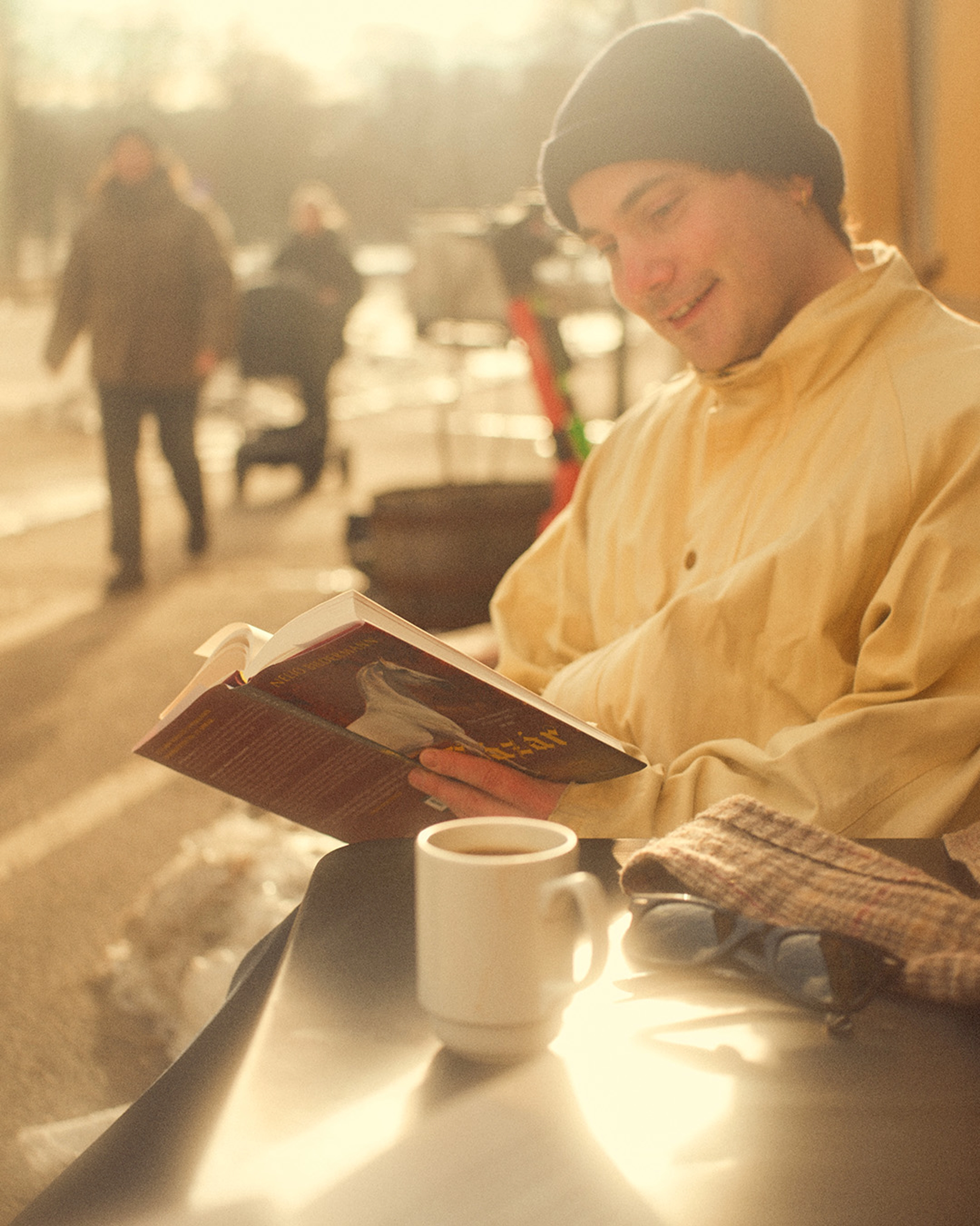 En mann sitter på en uteservering med kaffekopp og boka Lázár.