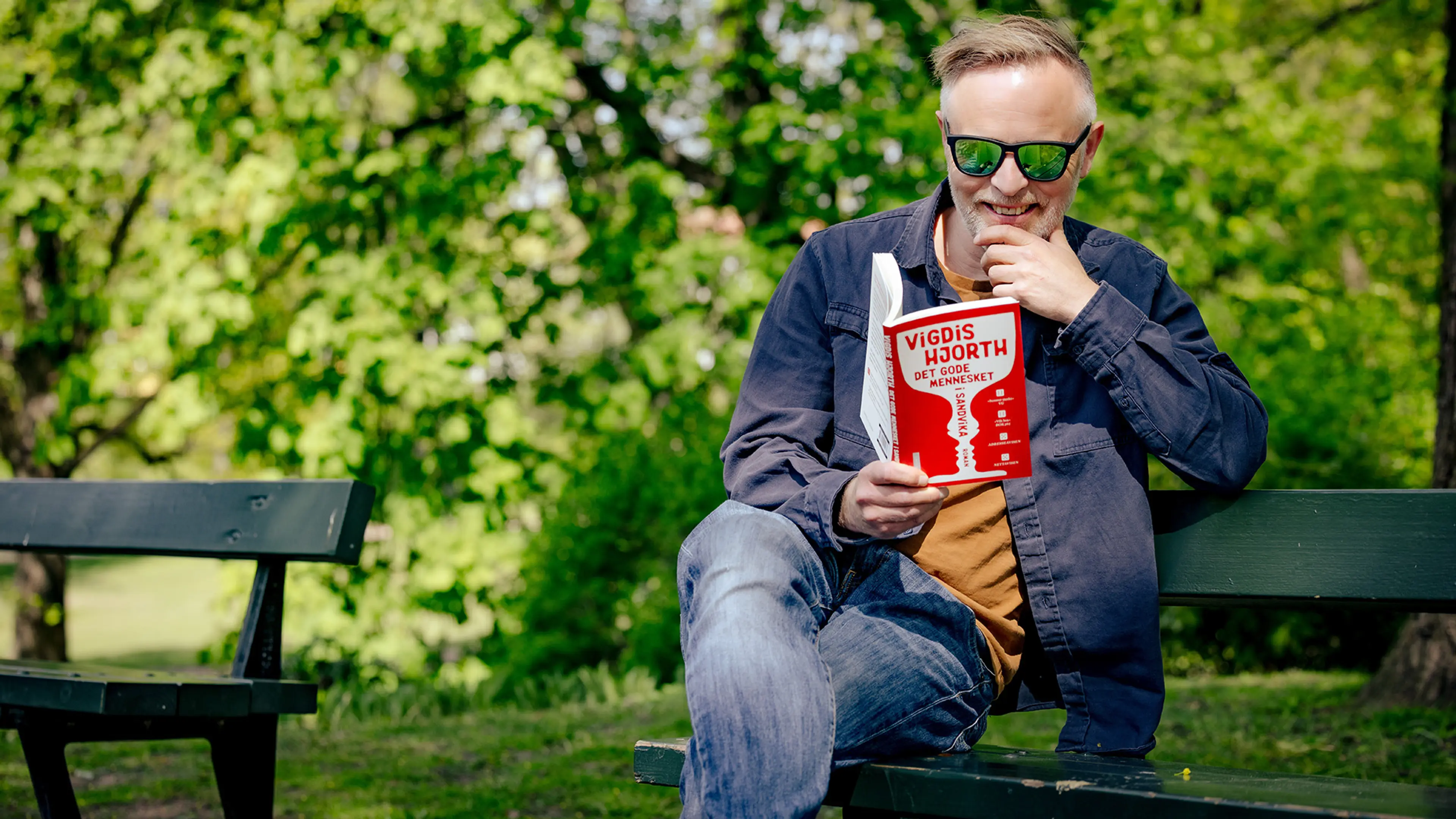 Mann som sitter på en benk og leser "Det gode mennesket i Sandvika"