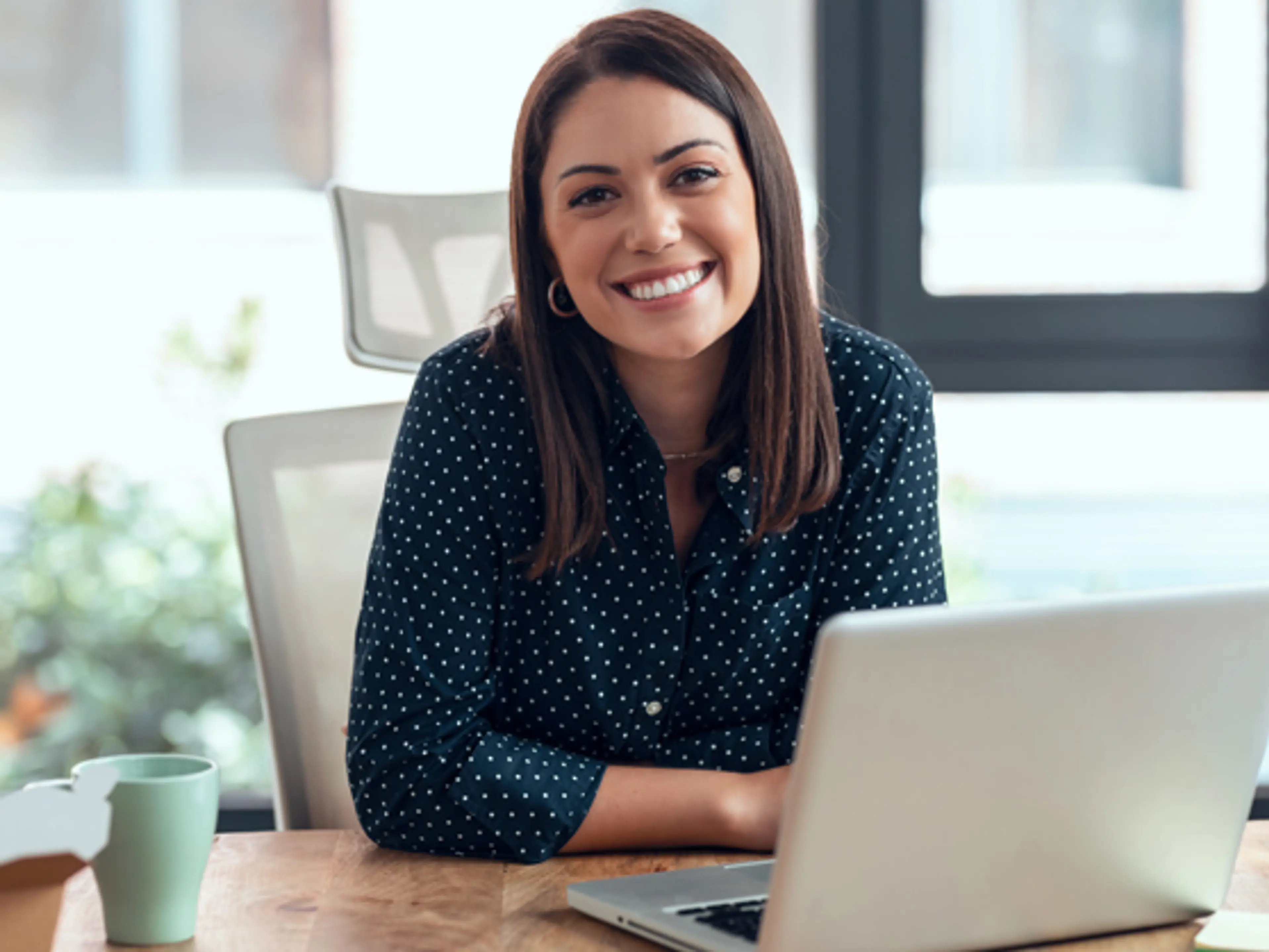 Smilende dame som sitter og jobber på en pc. Foto