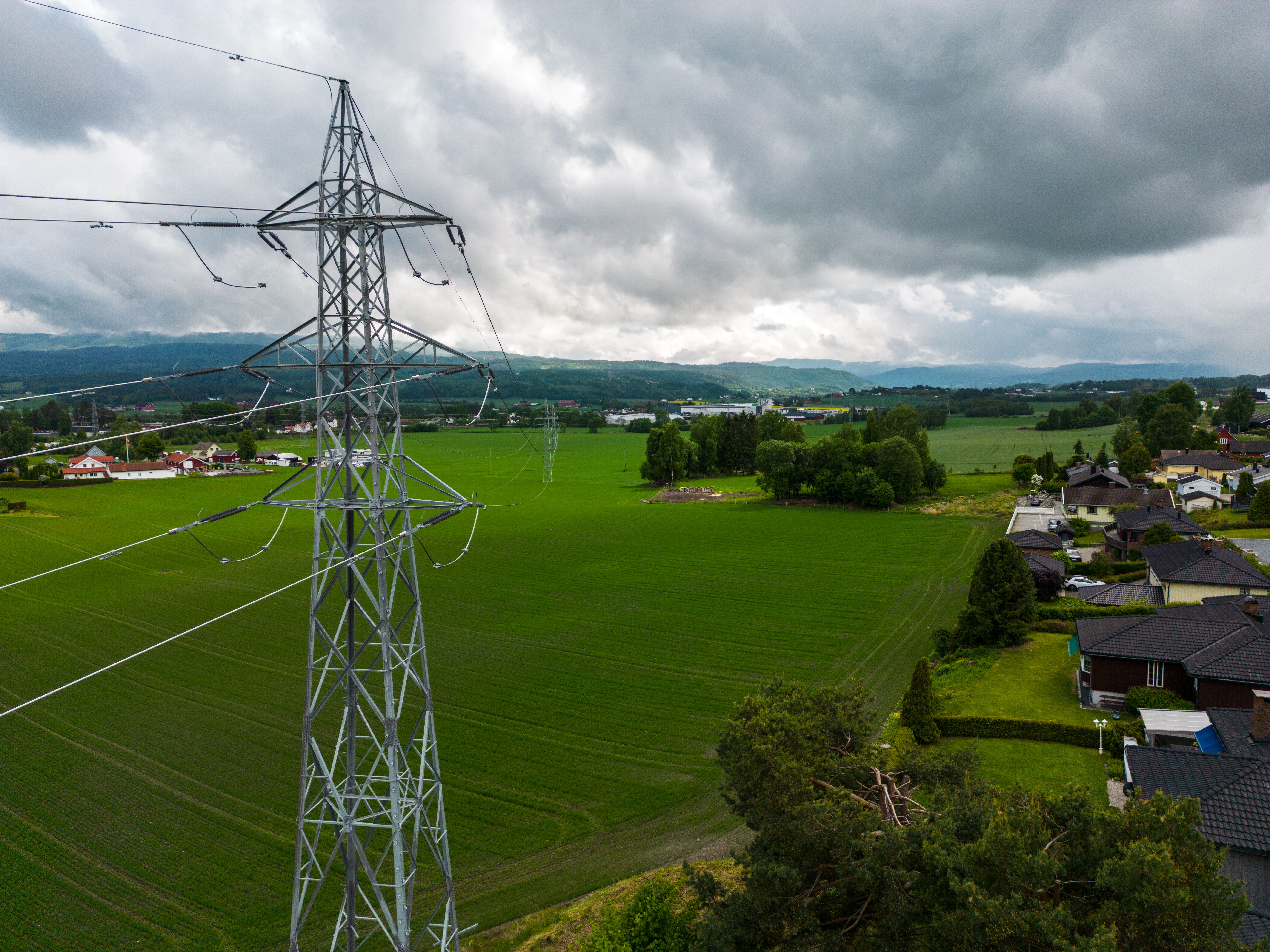 Høyspentmast med jorde og bebyggelse i bakgrunnen