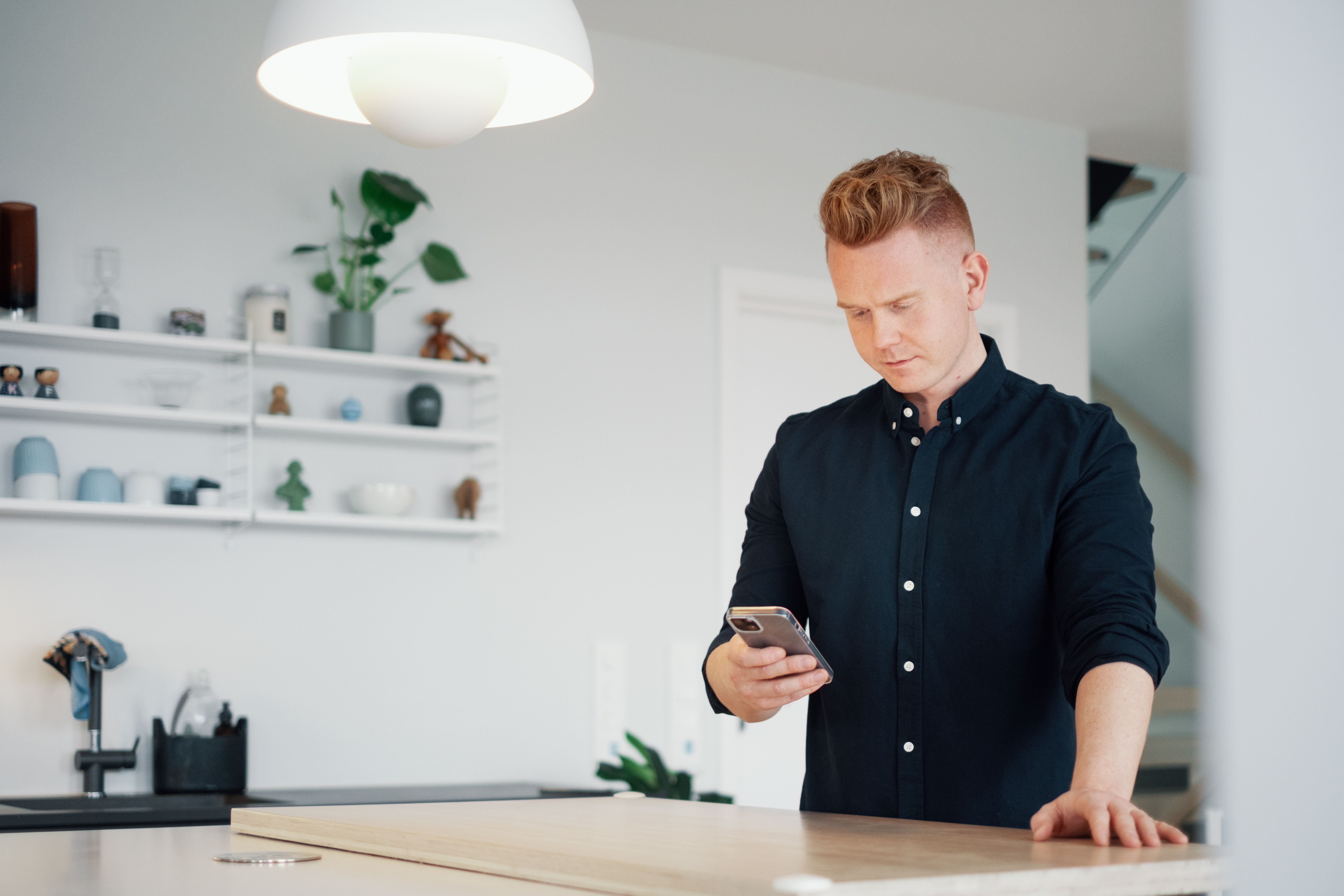 Mann leser på mobilen sin på kjøkkenet