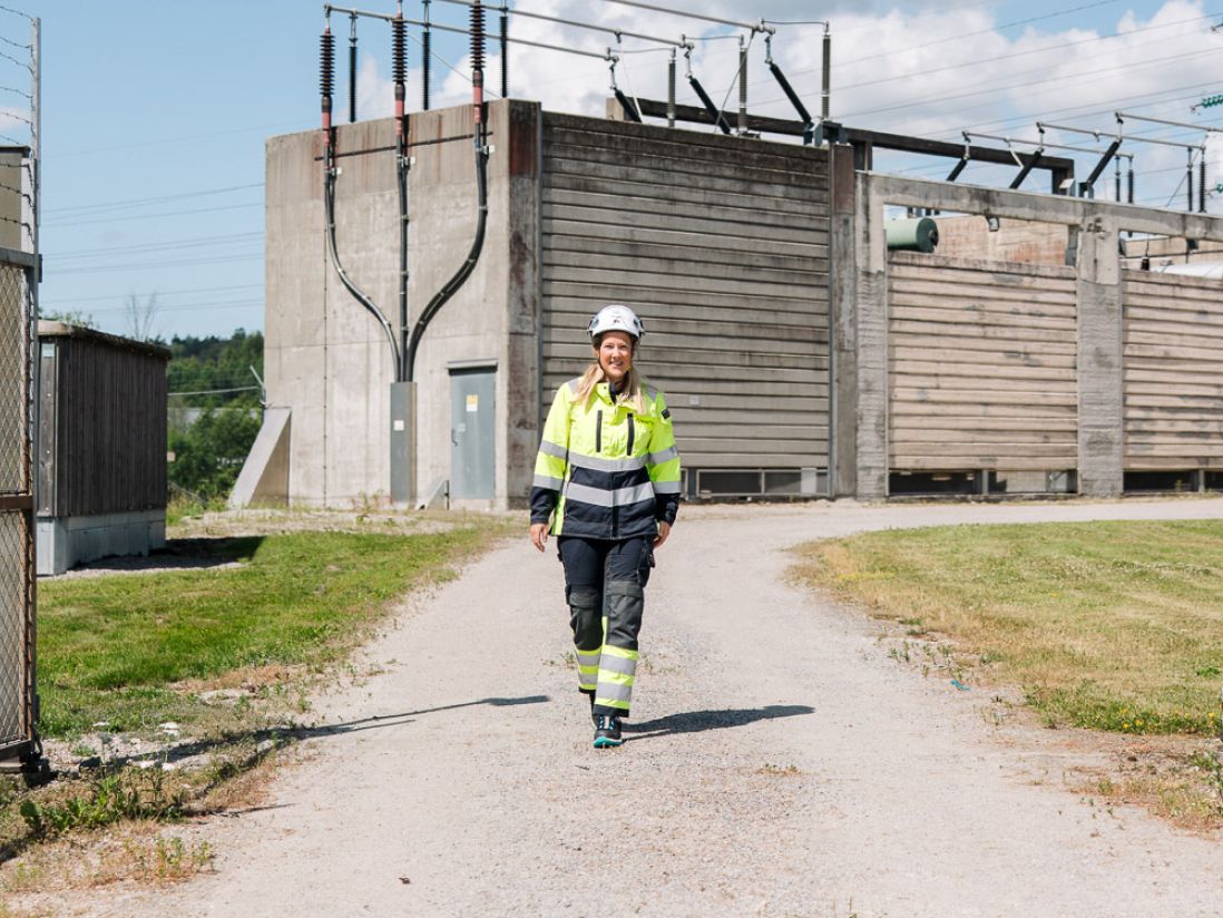 Dame i arbeidsklær som går smilende mot kamera