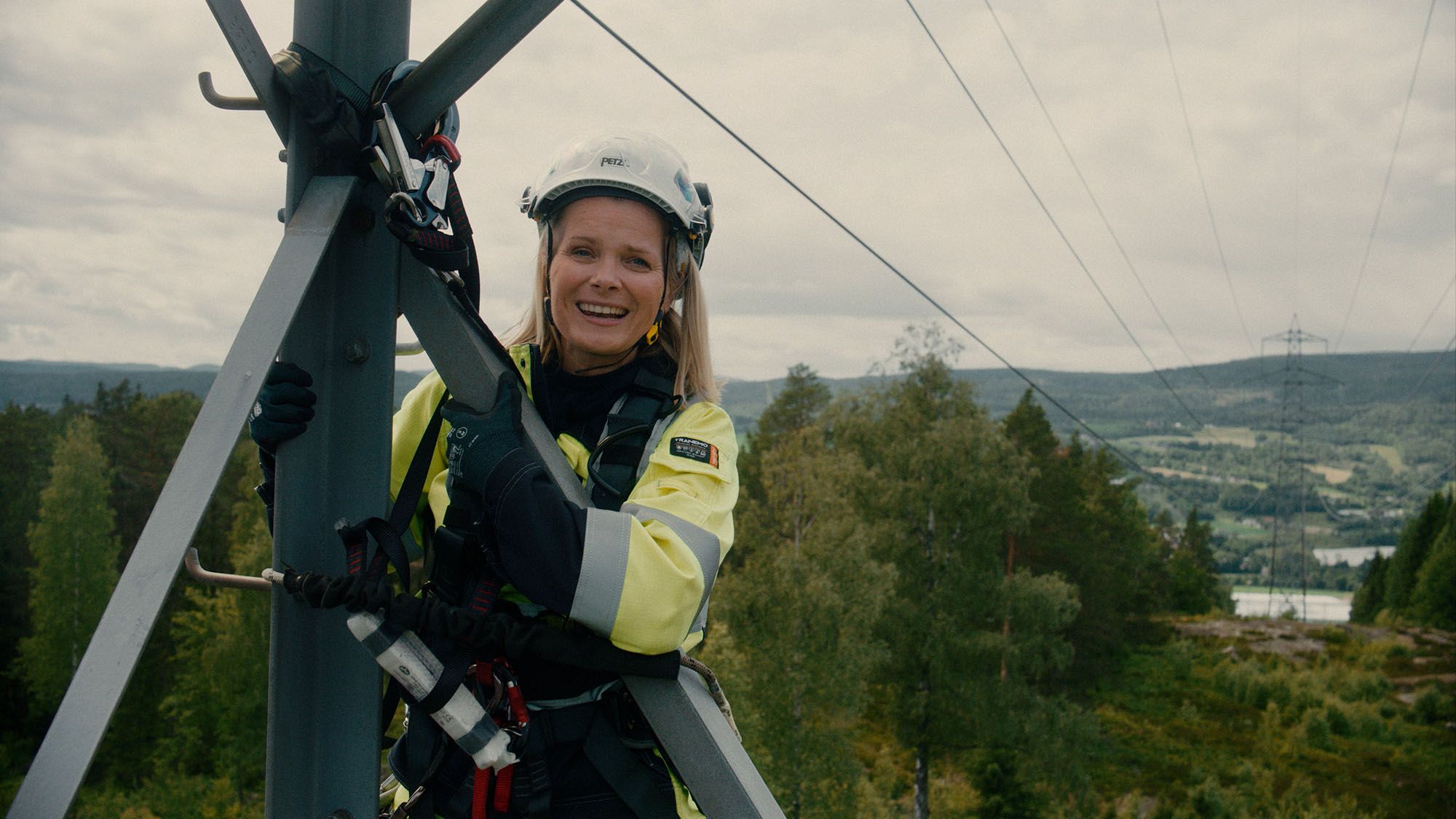 Nærbilde av dame i vernetøy og hjelm, oppe i en strømmast